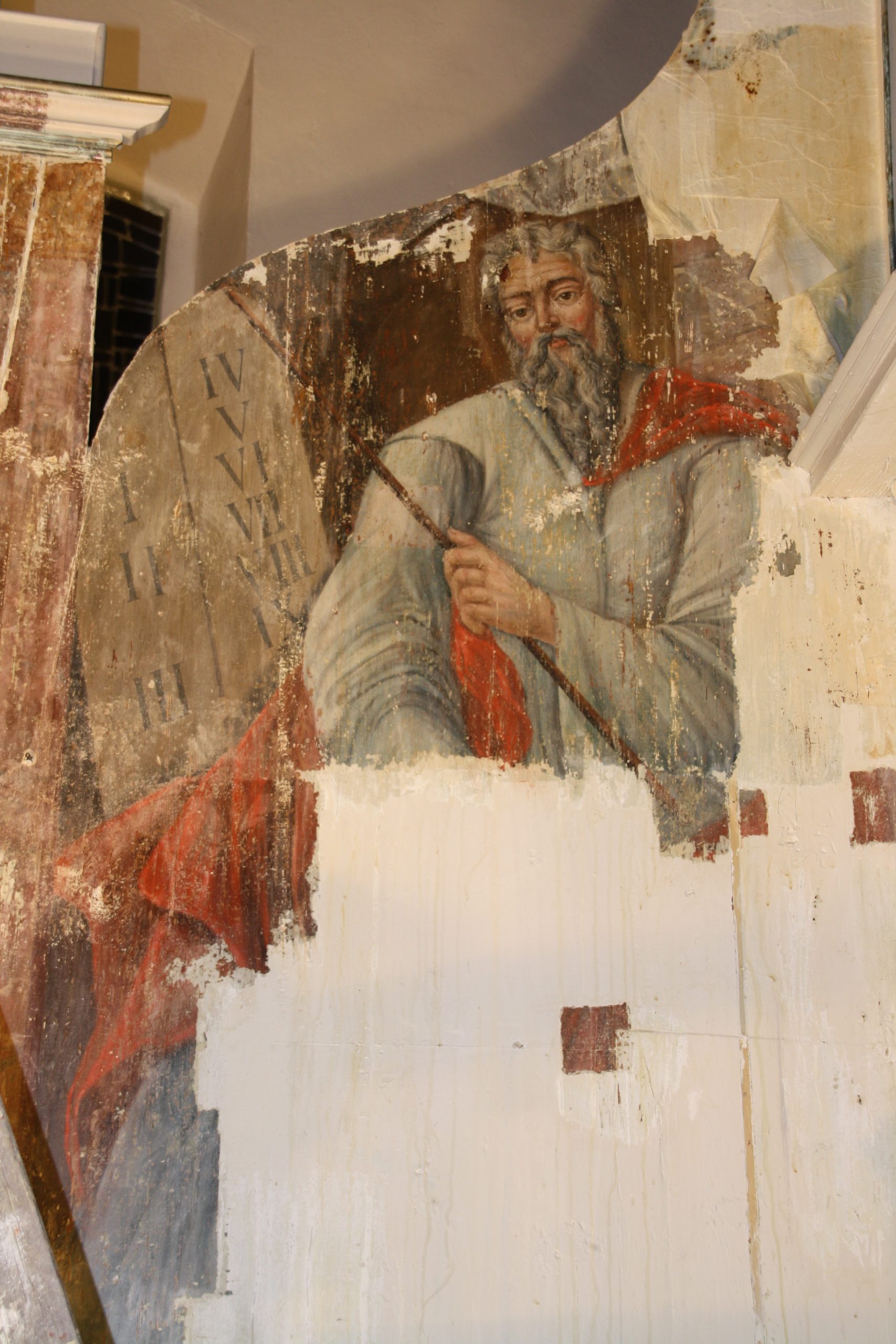 Early restoration stage of the altar wall painting depicting Moses with the Tablets of the Law, showing extensive overpaint, losses, and partially uncovered original paint